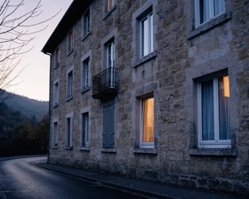 Immeuble de pierre au crepuscule, fenetres eclairees et un volet ferme